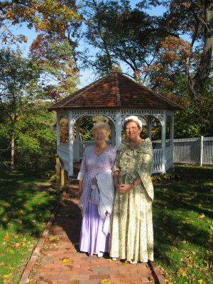 Two women in period costume standing on the path to the gazebo at Laurel Hill Mansion.