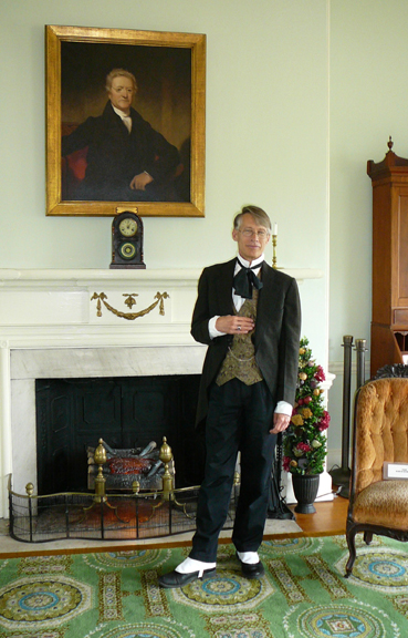 Fairmount Park guide Tyson Gardner in period costume stands in front of a portrait of William Rawle that hangs in Laurel Hill Mansion.